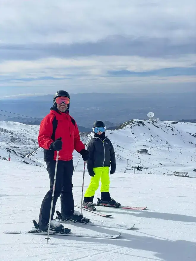 Niño con casco y gafas de esquí junto a un adulto en las pistas de Sierra Nevada