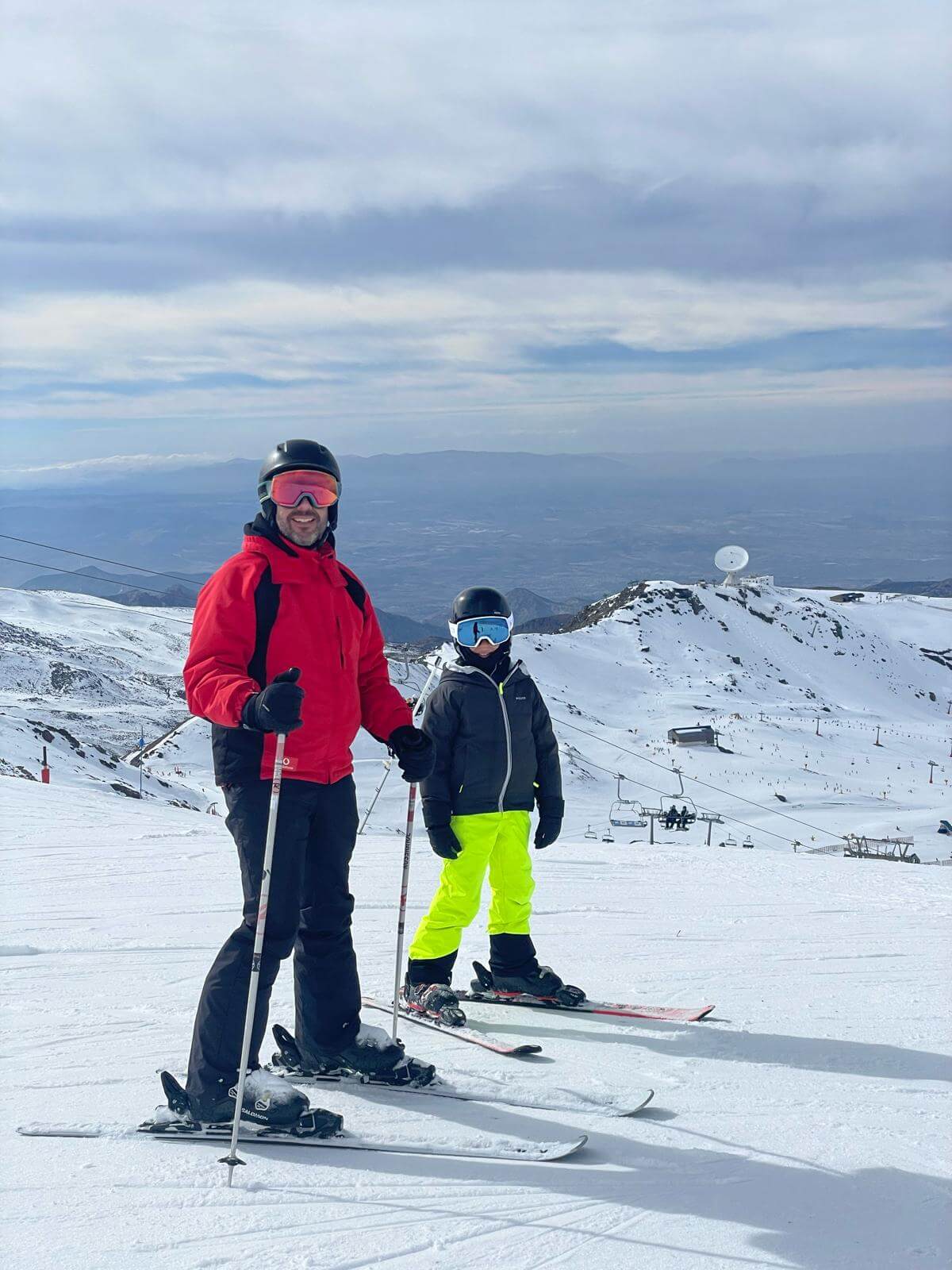 Niño con casco y gafas de esquí junto a un adulto en las pistas de Sierra Nevada