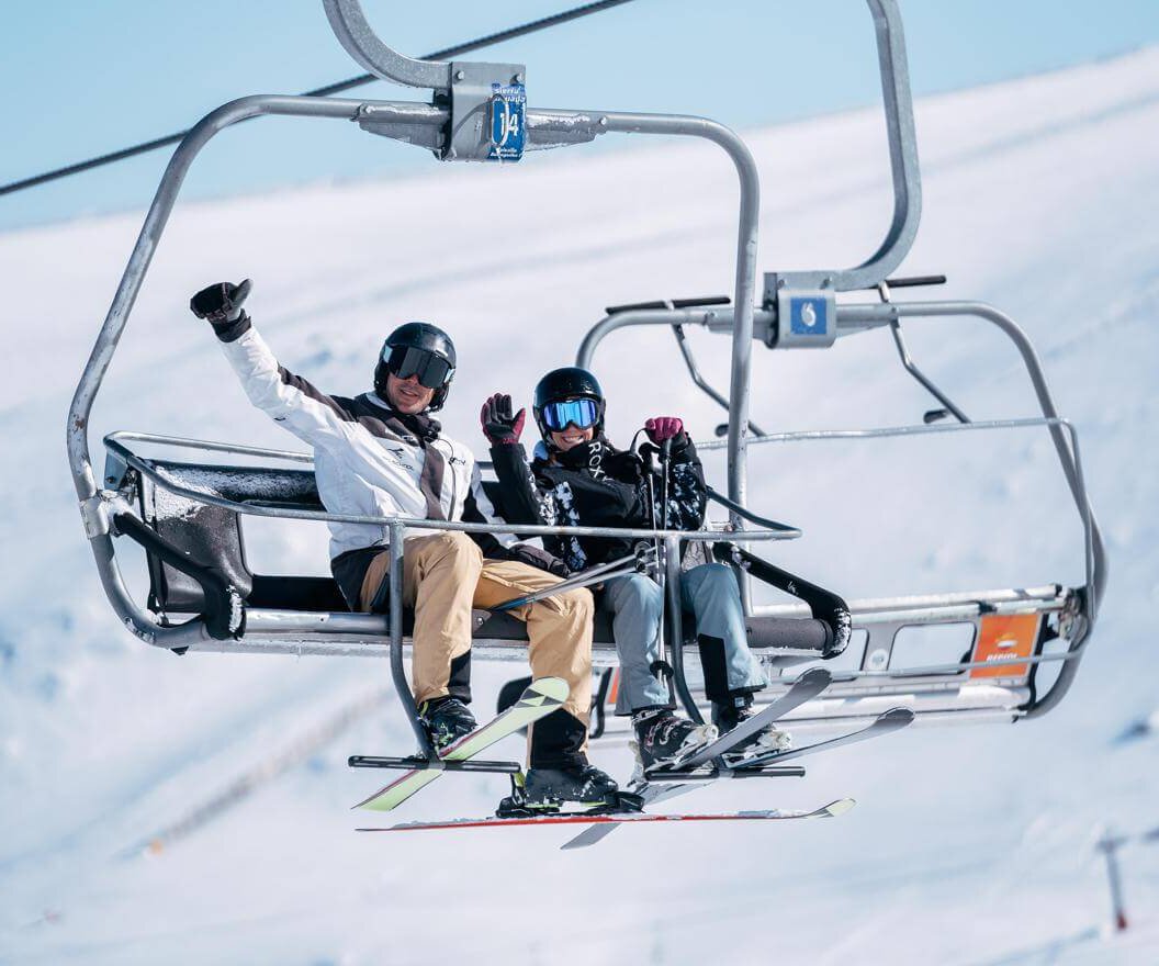 Dos esquiadores saludando desde un telesilla en Sierra Nevada